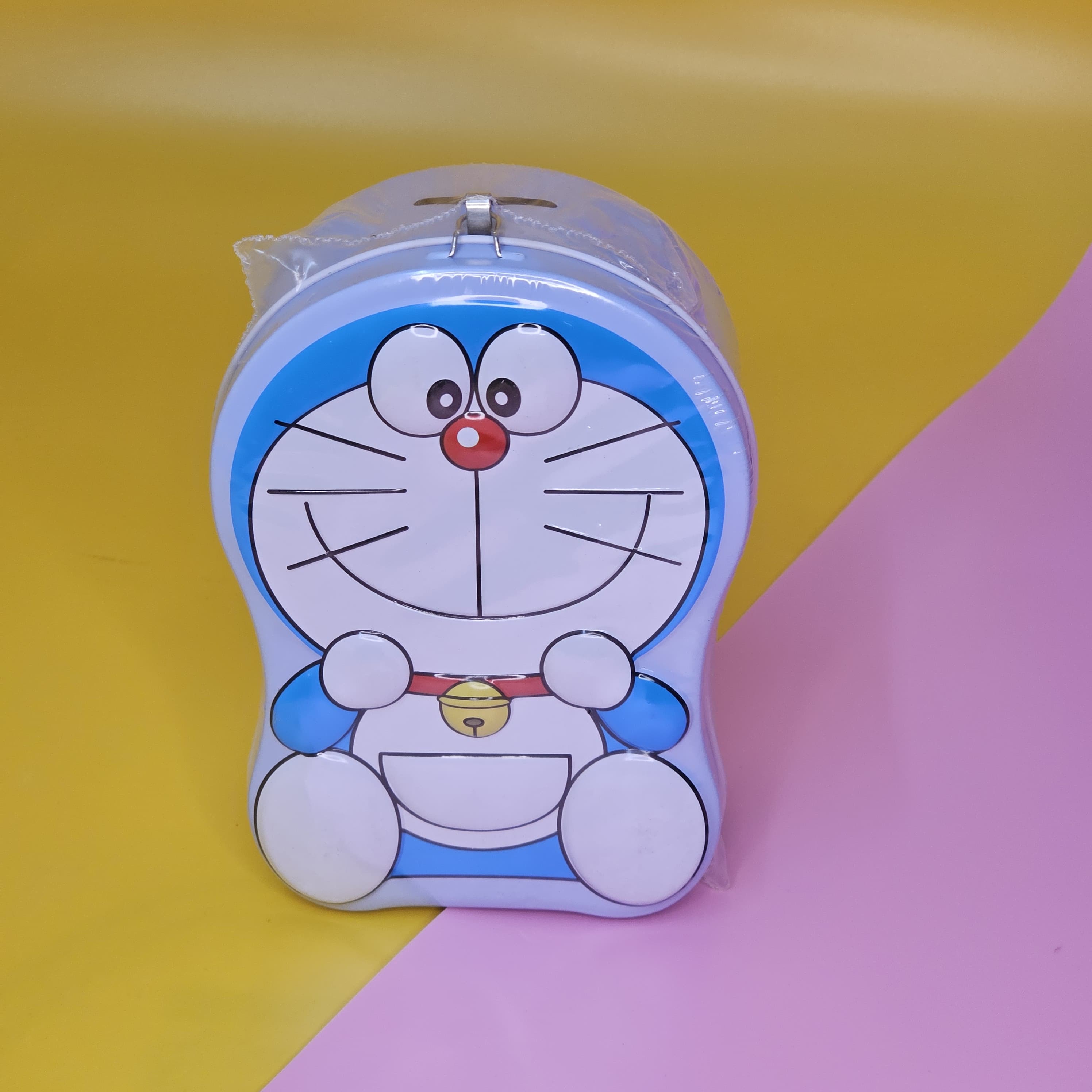 "Blue and white Doraemon-shaped metal money box (piggy bank) with a top slot for coins, featuring a lock and key for secure saving. Ideal gift for kids from uSmile.toys." www.usmile.toys